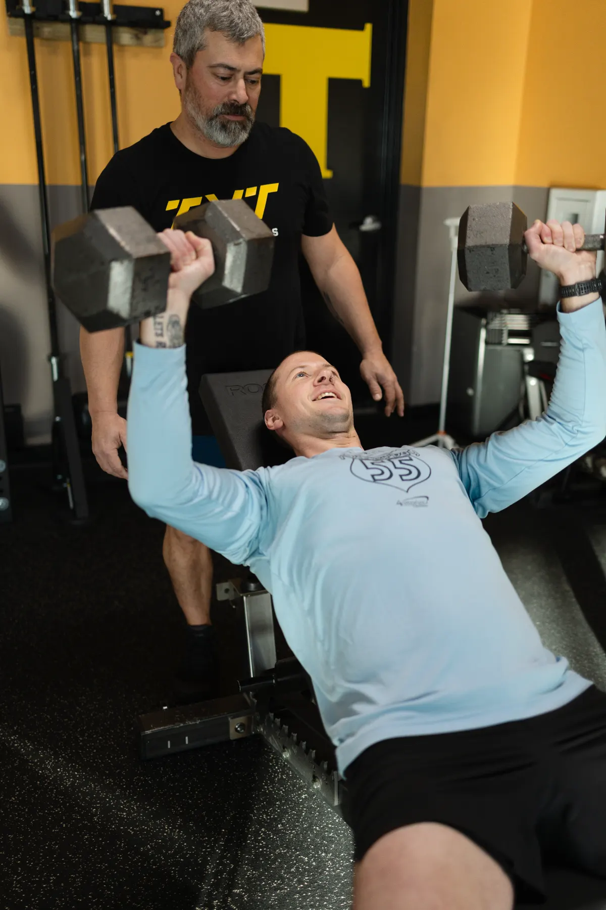 Coach spotting an adult member through a barbell bench press at TNT Fitness in Menasha